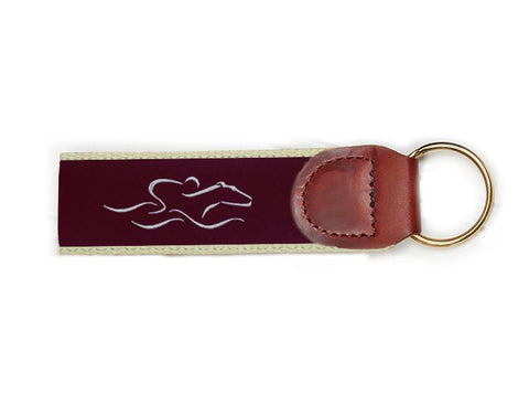 An EMBRACE THE RACE signature key fob with our signature cardinal and white ribbon on taupe backing and brown leather tab.