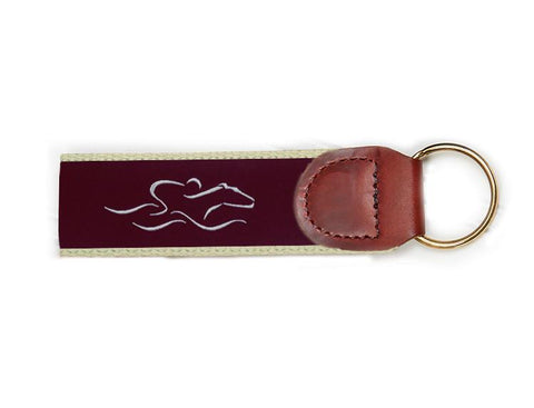 An EMBRACE THE RACE signature key fob with our signature cardinal and white ribbon on taupe backing and brown leather tab.  